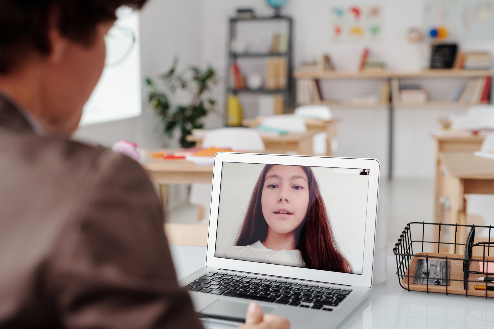 A teacher sitting at a classroom desk using a laptop to plan a lesson with an AI assistant visible on the screen