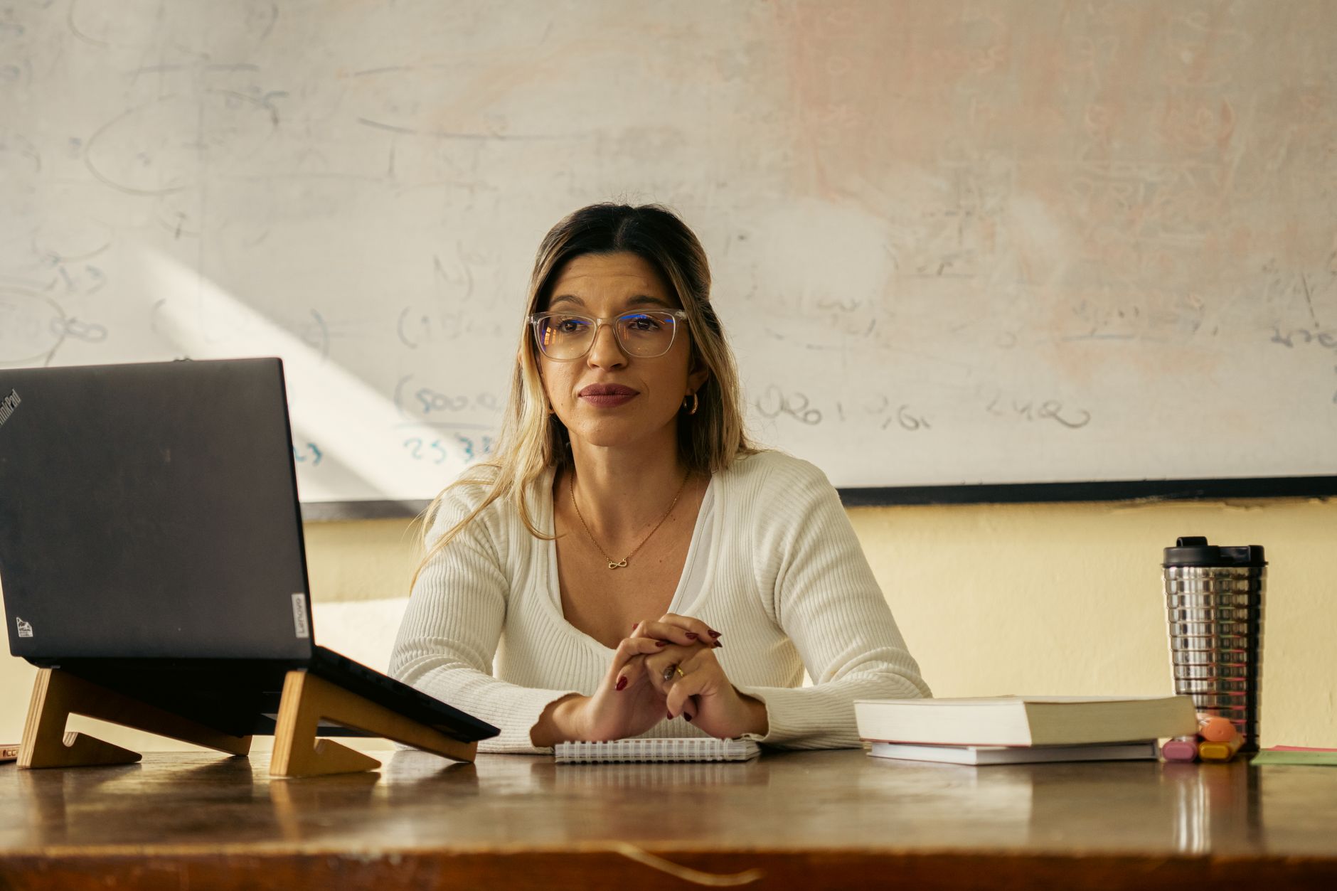 A teacher creating presentation slides on a laptop with printed study guide notes beside the laptop