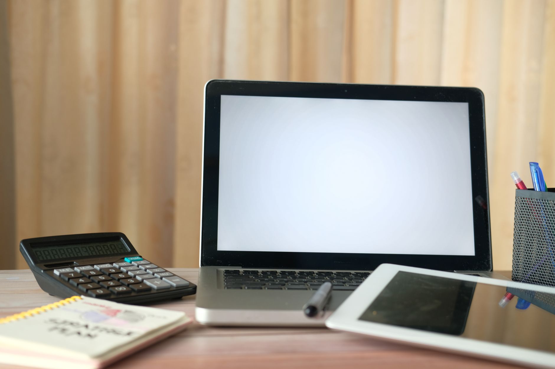 A notebook and pen rest beside a laptop screen glowing in a dim room.